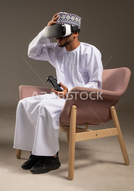 قضاء وقت ممتع ومسلي، محاكاة العالم الخيالي، التفاعل والاندماج مع ألعاب الفيديو، بورتريه لرجل عربي خليجي عماني يرتدي الدشداشة والكمة ونظارة الواقع الافتراضي يجلس على كرسي مريح يحمل عصا التحكم يضع يده على راسه بتعابير الخيبة والخسارة، خلفية بيضاء