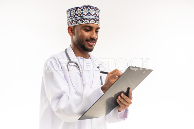 تدوين نتائج الفحوصات بالسجل الطبي، حسن التعامل مع المراجعين، ايماءات البشاشة والسرور، بورتريه مقرب لطبيب عربي خليجي عماني يرتدي الدشداشة والكمة والمعطف الأبيض يحمل بيده ملفات المرضى، إعداد التقارير الطبية، العمل في القطاع الصحي في سلطنة عمان، خلفية بيضاء