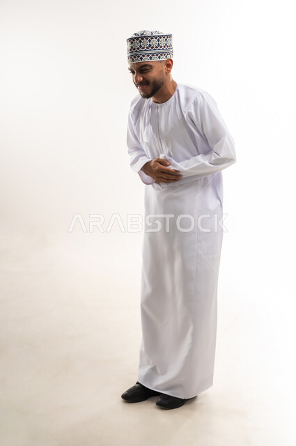 الإحساس بآلام في المعدة, طلب المساعدة للذهاب إلى الطبيب، الحاجة للدواء ووضع خطة علاجية, عسر الهضم والشعور بالمغص، بورتريه لرجل عربي خليجي عماني يرتدي الدشداشة والكمة يضع يديه على بطنه بإيماءات الألم, الجسم بالطول الكامل, خلفية بيضاء