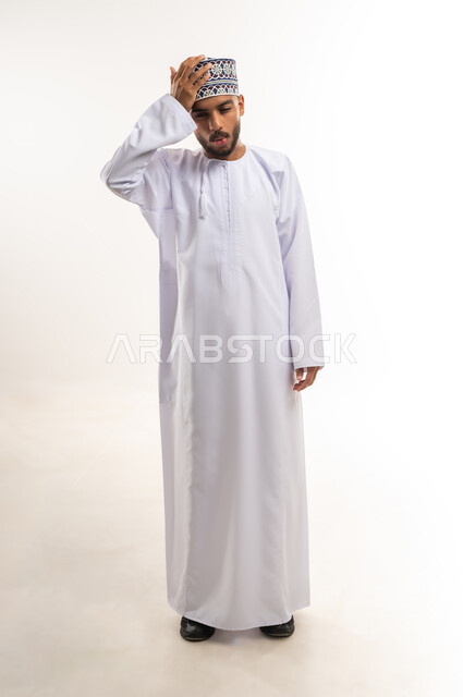 التذكر المفاجئ لشيء هام، التأخر على موعد ما, الإغفال والسهو والغفلة, بورتريه لرجل عربي عماني يرتدي الدشداشة والكمة يضع يده على رأسه بتعابير النسيان والذهول, الجسم بالطول الكامل, خلفية بيضاء