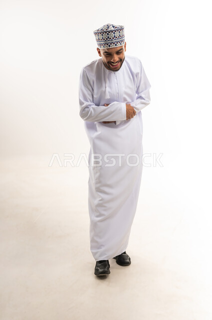 Feeling joyful and happy, expressions of extreme joy and pleasure, portrait of an Arab Gulf Omani man wearing a dishdasha and a kummah, putting his hand on his stomach with laughing gestures, full body length, white background