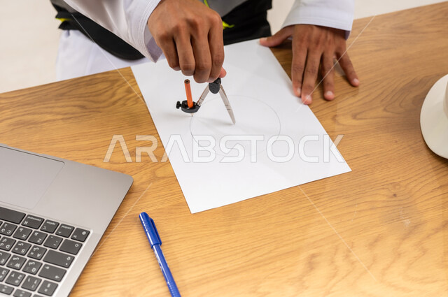 Using engineering tools and equipment, creating plans and construction projects, working in the engineering sector, integrating modern technologies into engineering work, close-up of an Arab Gulf Omani engineer wearing a safety vest drawing using compass