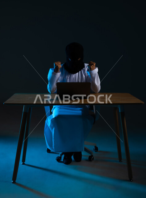 قرصنة وسرقة البيانات, التسلل عبر الأمن السيبراني, خوارزميات لتدمير الحسابات الرقمية, استخدم جهاز الحاسوب لأغراض غير قانونية, بورتريه لهاكر عربي خليجي عماني ملثم يرتدي الدشداشة يرفع قبضة يديه بتعابير الفرح لنجاح عملية الاختراق, خلفية زرقاء