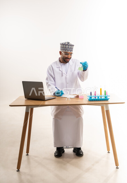 دمج الأجهزة الحديثة والتكنولوجيا في الحياة العملية, القيام بالتجارب والبحوث العلمية, مفهوم الكيمياء الحيوية, بورتريه لأخصائي مختبر عربي خليجي عماني يرتدي المعطف الأبيض والكمة يقوم باستعمال أنابيب الاختبار, خلفية بيضاء