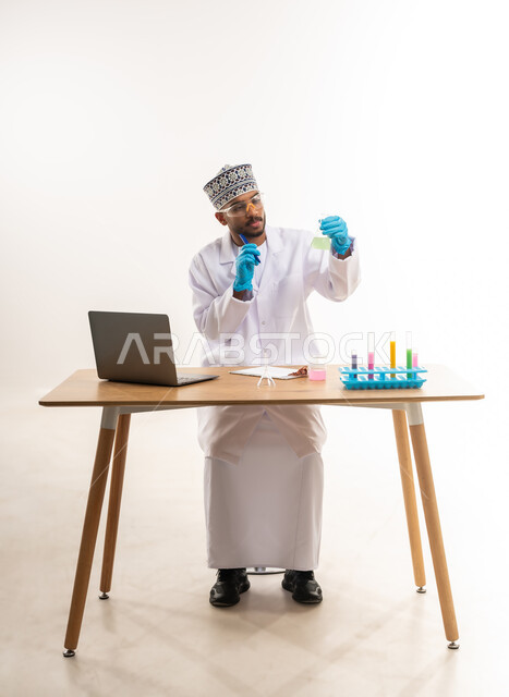دمج الأجهزة الحديثة والتكنولوجيا في الحياة العملية, القيام بالتجارب والبحوث العلمية, مفهوم الكيمياء الحيوية, بورتريه لمخبري عربي خليجي عماني يرتدي المعطف الأبيض والكمة يقوم باستعمال أنابيب الاختبار, خلفية بيضاء