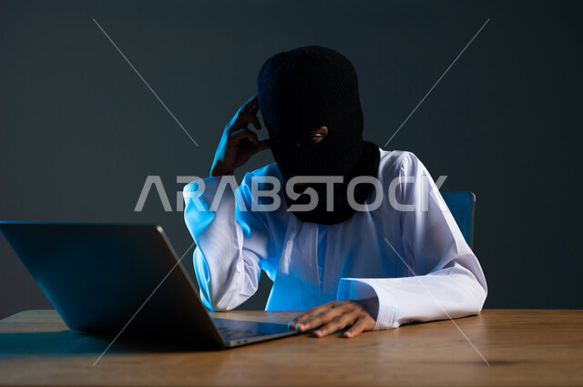 قرصنة وسرقة البيانات, تدمير الحسابات الرقمية, استخدم جهاز الحاسوب لأغراض غير مشروعة، مفهوم الجرائم الالكترونية, القدرة على تهكير الأجهزة, بورتريه مقرب لهاكر عربي خليجي عماني ملثم يرتدي الدشداشة يضع يده على رأسه بتعابير التمعن والتركيز، خلفية رمادية