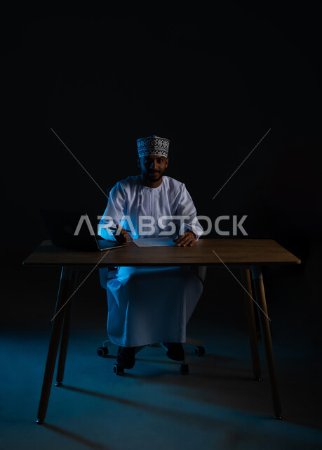 Planning to hack and steal data, hacking systems and device security, algorithms to destroy digital accounts, using a laptop for illegal purposes, portrait of an Arab Gulf Omani hacker wearing a dishdasha and a cloak writing on a white paper, black background