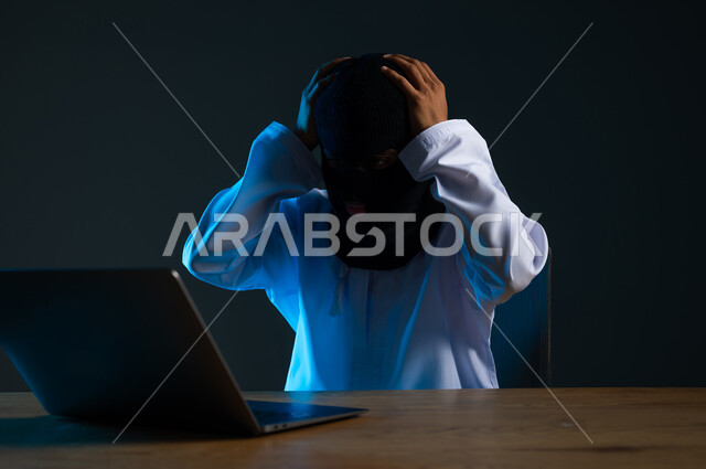 تدمير الحسابات الرقمية, استخدم جهاز الحاسوب لأغراض غير مشروعة، مفهوم الجرائم الالكترونية, القدرة على تهكير الأجهزة, قرصنة وسرقة البيانات, بورتريه مقرب لهاكر عربي خليجي عماني ملثم يرتدي الدشداشة يضع يديه على رأسه بتعابير الانزعاج، خلفية رمادية