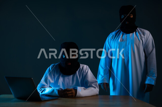 التسلل عبر الأمن السيبراني, استخدم جهاز الحاسوب لأغراض غير قانونية، قرصنة وسرقة البيانات, خوارزميات لتدمير الحسابات الرقمية, بورتريه مقرب لهكرين عربيين خليجيين عمانيين ملثمين يرتديان الدشداشة يعملان في مجال الهكر, خلفية زرقاء