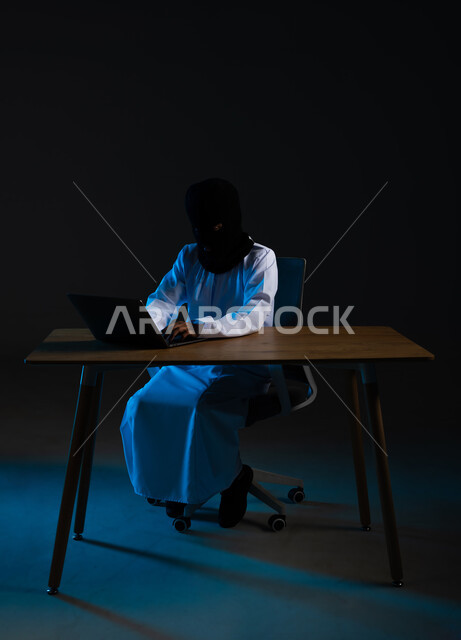 Use of computer for illegal purposes, concept of cybercrime, ability to hack devices, hacking and stealing data, destruction of digital accounts, portrait of a masked Arab Gulf Omani hacker wearing a dishdasha working in the field of illegal hacking, black background