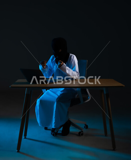 Hacking and data theft, cyber security intrusion, algorithms to destroy digital accounts, use of laptop for illegal purposes, portrait of a masked Arab Gulf Omani hacker wearing a dishdasha raising his fist with gestures of joy for the success of the hacking operation, blue background