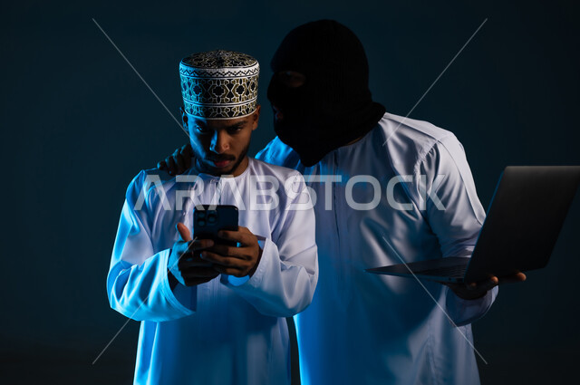 التجسس على المحادثات والحسابات الشخصية, سرقة وقرصنة البيانات الالكترونية, اختراق الأنظمة وحماية وأمن الأجهزة, التعرض للهجمات والاختراقات, بورتريه مقرب لهاكر يستخدم جهاز الحاسوب لاختراق هاتف رجل عربي خليجي عماني يرتدي الدشداشة والكمة، خلفية زرقاء