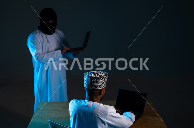 تدمير الحسابات الرقمية, التسلل عبر الأمن السيبراني، قرصنة وسرقة البيانات الشخصية, التعرض للهجمات والاختراقات، اختراق حماية وأمن وخصوصية المستخدمين, بورتريه لهاكر يستخدم الحاسوب المحمول لاختراق جهاز رجل عربي خليجي عماني يرتدي الدشداشة والكمة, خلفية زرقاء