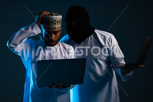 قرصنة وسرقة البيانات الشخصية, التعرض للهجمات والاختراقات، اختراق حماية وأمن وخصوصية المستخدمين, تدمير الحسابات الرقمية, التسلل عبر الأمن السيبراني, بورتريه مقرب لهاكر يستخدم الحاسوب المحمول لاختراق جهاز رجل عربي خليجي عماني يرتدي الدشداشة والكمة, خلفية زرقاء