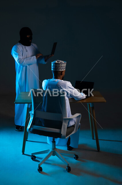 Data hacking and theft, exposure to attacks and breaches, breach of user protection and security, concept of cybercrime, ability to hack devices, portrait of a hacker using a laptop to hack the device of an Arab Gulf Omani man wearing a dishdasha and a keffiyeh, blue background