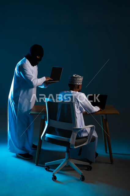 Hacking systems and protecting and securing devices, exposure to attacks and hacking, data theft and piracy, portrait of a hacker using a laptop to hack the device of an Arab Gulf Omani man wearing a dishdasha and a turban, displaying a blank black screen via computer, blue background