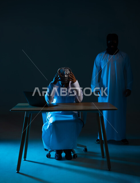 قرصنة وسرقة البيانات, التعرض للهجمات والاختراقات، اختراق حماية وأمن المستخدمين، مفهوم الجرائم الالكترونية, بورتريه لرجل عربي خليجي عماني يرتدي الدشداشة والكمة يستعمل الحاسوب المحمول يضع يده على رأسه ويقف خلفه المخترق, خلفية زرقاء
