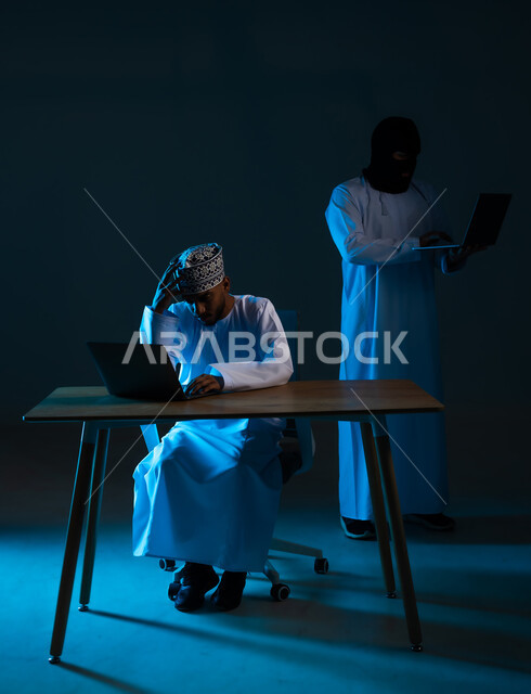 التعرض للهجمات والاختراقات, قرصنة وسرقة البيانات، اختراق حماية وأمن المستخدمين، مفهوم الجرائم الالكترونية, بورتريه لهاكر يستخدم الحاسوب المحمول لاختراق جهاز رجل عربي خليجي عماني يرتدي الدشداشة والكمة, خلفية زرقاء
