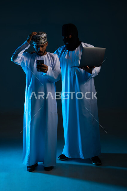 Successful hacking of users' security and privacy, ability to hack devices, exposure to attacks and hacks, portrait of a hacker using a computer to hack the phone of an Arab Gulf Omani man wearing a dishdasha and a kimono, full-length body, blue background