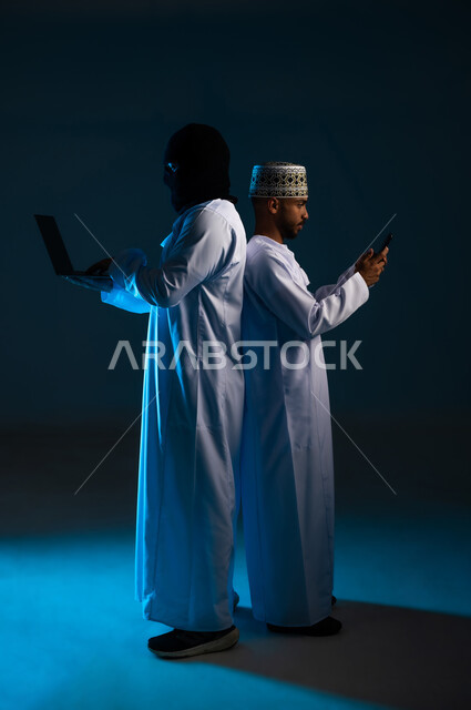 Hacking protection, security and privacy of users, concept of cybercrime, ability to hack devices, exposure to attacks and hacks, side portrait of a hacker using a computer to hack the phone of an Arab Gulf Omani man wearing a dishdasha and a kimono, full body, blue background