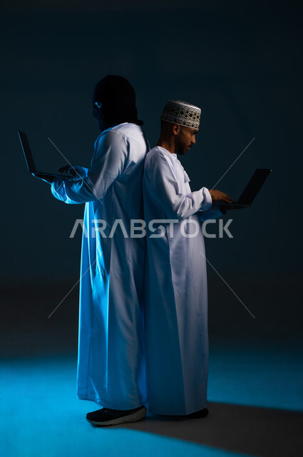 التعرض للهجمات والاختراقات، اختراق حماية وأمن وخصوصية المستخدمين، مفهوم الجرائم الالكترونية, القدرة على تهكير الأجهزة, بورتريه من الجانب لهاكر يستخدم الحاسوب المحمول لاختراق جهاز رجل عربي خليجي عماني يرتدي الدشداشة والكمة، الجسم بالطول الكامل, خلفية زرقاء
