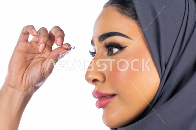 بورتريه لمرأة عربية خليجية سعودية تضع رموش اصطناعية للحصول على رموش طويلة وكثيفة ، خلفية بيضاء لمرأة خبيرة بمستحضرات التجميل، التسويق لمنتجات التجميل، متجر بيع مستحضرات التجميل عبر الإنترنت ، مفهوم الإهتمام بالجمال الخارجي ومظهر العينين