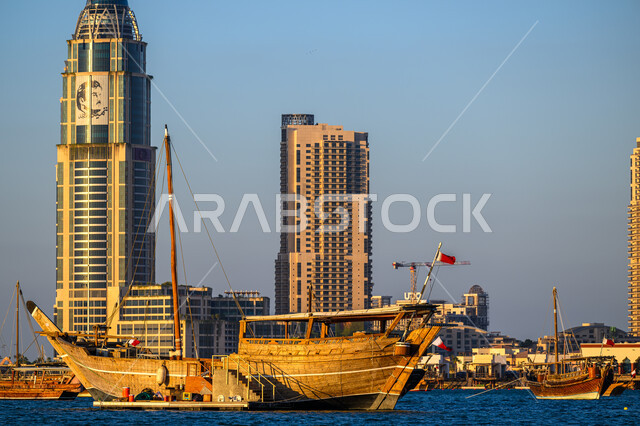 قارب خشبي وسط البحر على كورنيش مدينة الدوحة، الاستمتاع بالرحلات و النزهات البحرية الهادئة، مهرجان كتارا الرابع عشر للمحامل، الواجهة البحرية في دولة قطر في النهار، أماكن سياحية لقضاء أوقات ممتعة