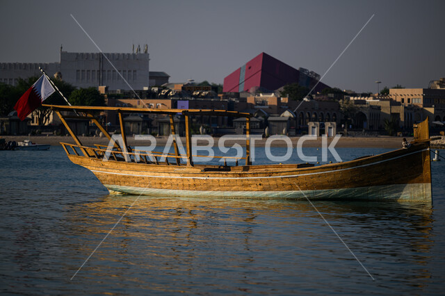 الاستمتاع بالرحلات و النزهات البحرية الهادئة، مهرجان كتارا الرابع عشر للمحامل، الواجهة البحرية في دولة قطر في النهار، أماكن سياحية لقضاء أوقات ممتعة، قارب خشبي وسط البحر على كورنيش مدينة الدوحة