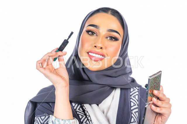بورتريه لمرأة عربية خليجية سعودية تحمل إحدى أدوات التجميل (قلم المسكرة) لإبراز العين ، خلفية بيضاء لمرأة خبيرة بمستحضرات التجميل، التسويق لمنتجات التجميل، متجر بيع مستحضرات التجميل عبر الإنترنت ، مفهوم الإهتمام بالجمال والبشرة، ادوات مكياج تتوريال