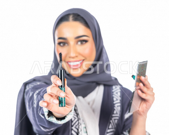 بورتريه لمرأة عربية خليجية سعودية تحمل إحدى أدوات التجميل (قلم المسكرة) لإبراز العين ، خلفية بيضاء لمرأة خبيرة بمستحضرات التجميل، التسويق لمنتجات التجميل، متجر بيع مستحضرات التجميل عبر الإنترنت ، مفهوم الإهتمام بالجمال والبشرة، ادوات مكياج تتوريال