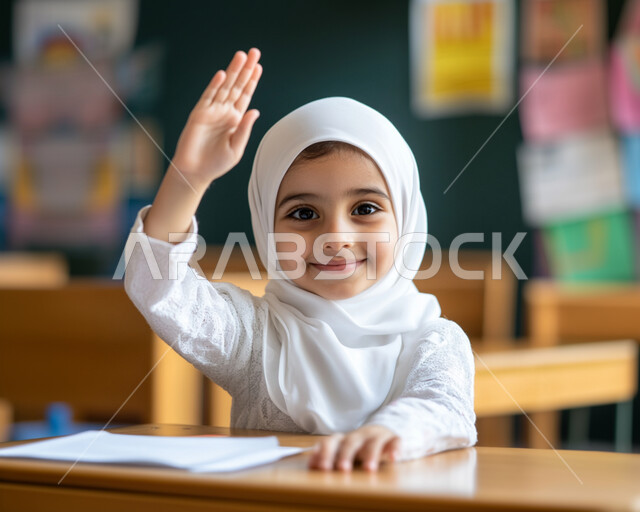 ايماءات الحماس لمعرفة الجواب الصحيح، المشاركة والتفاعل داخل الفصل الدراسي، صورة مقربة لطالبة عربية خليجية سعودية محجبة مبتسمة تجلس على المقعد ترفع يدها للإجابة على السؤال، التربية والتعليم بالمناهج المقررة للطلاب في المملكة