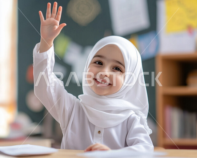 التربية والتعليم بالمناهج المقررة للطلاب في المملكة، ايماءات الحماس لمعرفة الجواب الصحيح، المشاركة والتفاعل داخل الفصل الدراسي، صورة مقربة لطالبة عربية خليجية سعودية محجبة مبتسمة تجلس على المقعد ترفع يدها للإجابة على السؤال
