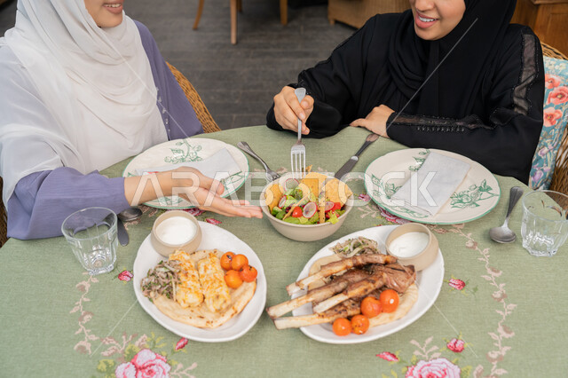 قضاء وقت ممتع ومسلي مع الاصدقاء, الاستمتاع بتناول الأطباق الشهية، شابتان سعوديتان تتناولان الطعام، تشكيلة متنوعة من المأكولات على السفرة، شابة عربية خليجية اماراتية محجبة تتناول الغداء في المطعم برفقة صديقتها، المطاعم و الكافيهات في الإمارات