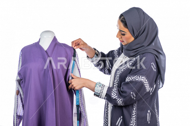 بورتريه لمصممة أزياء خليجية سعودية تعمل على أخذ القياسات بإستخدام الشريط المتري، مصممة أزياء مبتكرة، ورشة عمل تصميم ازياء، أدوات الخياطة، مهن وأعمال فن الخياطة، فنون ومهارات تصميم وتفصيل الملابس النسائية ، مفهوم عالم الأزياء والموضة، خلفية بيضاء