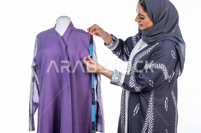 بورتريه لمصممة أزياء خليجية سعودية تعمل على أخذ القياسات بإستخدام الشريط المتري، مصممة أزياء مبتكرة، ورشة عمل تصميم ازياء، أدوات الخياطة، مهن وأعمال فن الخياطة، فنون ومهارات تصميم وتفصيل الملابس النسائية ، مفهوم عالم الأزياء والموضة، خلفية بيضاء