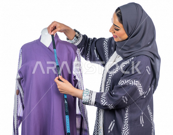 بورتريه لمصممة أزياء خليجية سعودية تعمل على أخذ القياسات بإستخدام الشريط المتري، مصممة أزياء مبتكرة، ورشة عمل تصميم ازياء، أدوات الخياطة، مهن وأعمال فن الخياطة، فنون ومهارات تصميم وتفصيل الملابس النسائية ، مفهوم عالم الأزياء والموضة، خلفية بيضاء