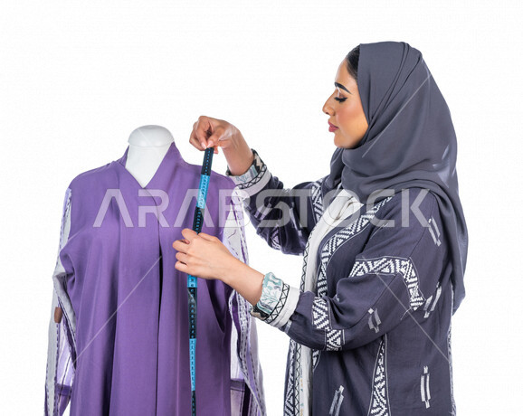 بورتريه لمصممة أزياء خليجية سعودية تعمل على أخذ القياسات بإستخدام الشريط المتري، مصممة أزياء مبتكرة، ورشة عمل تصميم ازياء، أدوات الخياطة، مهن وأعمال فن الخياطة، فنون ومهارات تصميم وتفصيل الملابس النسائية ، مفهوم عالم الأزياء والموضة، خلفية بيضاء