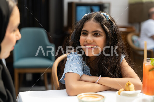 قضاء أوقات ممتعة في الخارج، استغلال وقت الفراغ في التسلية مع الاسرة، أجواء عائلية سعيدة مليئة بالحب والحنان، صورة مقربة لفتاة عربية خليجية اماراتية تنظر لوالدتها بايماءات السرور والسعادة، بنت سعودية تجلس في احدى الكافيهات