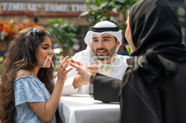 ايماءات السرور والسعادة، التسلية والترفيه بالعطلات، أجواء اسرية سعيدة مليئة بالحب، انشطة وفعاليات ترفيهية عائلية، مفهوم الألفة والمحبة بين أفراد الأسرة، صورة مقربة من الخلف لام عربية خليجية اماراتية تجلس في المقهى تقوم بتقديم الحلويات لابنتها، قضاء الوقت في الخارج