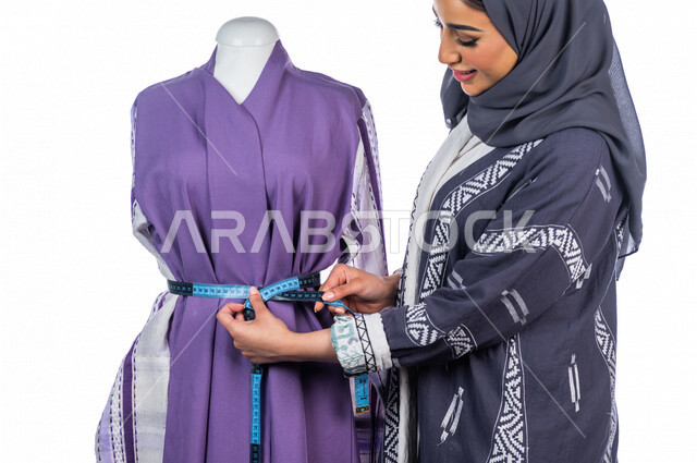 بورتريه لمصممة أزياء خليجية سعودية تعمل على أخذ القياسات بإستخدام الشريط المتري، مصممة أزياء مبتكرة، ورشة عمل تصميم ازياء، أدوات الخياطة، مهن وأعمال فن الخياطة، فنون ومهارات تصميم وتفصيل الملابس النسائية ، مفهوم عالم الأزياء والموضة، خلفية بيضاء