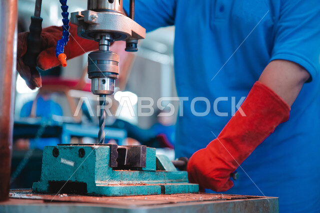 المهارة في اتقان العمل في مصنع الحداده, صورة مقربة لمهندس صناعي عربي خليجي سعودي يرتدي اليونيفورم والقفازات يقوم بلحام المعدن, تجهيز وتوصيل الحديد بمعدات وأدوات لحامية, مهن وأعمال سعوديه