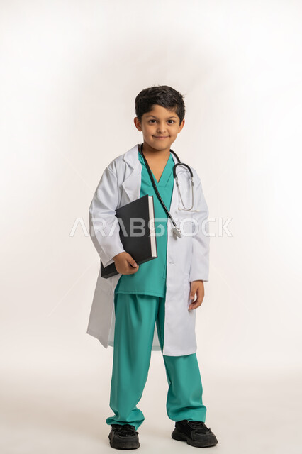 الهدف والطموح المستقبلي بالعمل في العيادات والمشافي، تحديد مهنة المستقبل، مفهوم الطب والرعاية الصحية، بورتريه لولد عربي خليجي اماراتي يرتدي المعطف الأبيض يضع السماعة الطبية يحلم بالعمل كطبيب، فتى سعودي يحمل بيده سجل المرضى، صورة لكامل الجسم، خلفية بيضاء