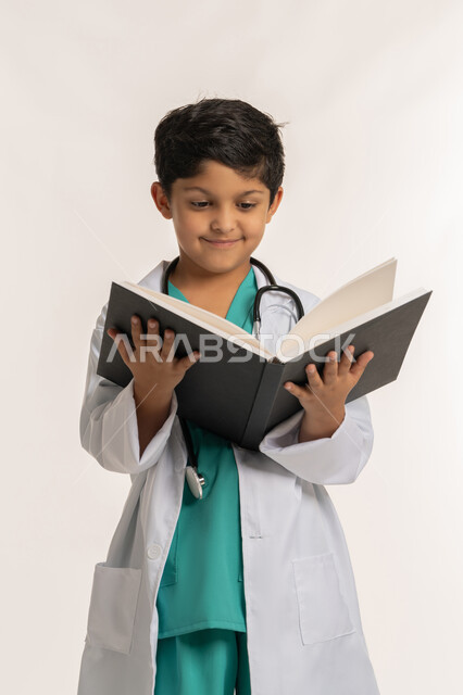 الاجتهاد للوصول إلى الغايات، الهدف والطموح المستقبلي بالعمل في العيادات والمشافي، مفهوم الطب والرعاية الصحية، بورتريه لولد عربي خليجي اماراتي يرتدي المعطف الأبيض يضع السماعة الطبية يحمل بيده سجل المرضى، فتى سعودي يقوم بالقراءة بايماءات التركيز، خلفية بيضاء