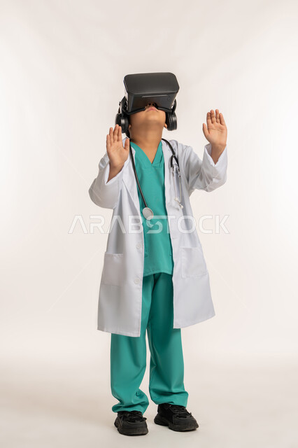 دمج التقنيات الحديثة بالمجال الطبي، مفهوم الطب والرعاية الصحية، بورتريه لولد عربي خليجي اماراتي يرتدي المعطف الأبيض يضع نظارة الفي ار يقوم بالتفاعل مع الواقع الافتراضي، صبي سعودي يرفع يديه بايماءات الاندماج مع العالم الخيالي، صورة لكامل الجسم، خلفية بيضاء