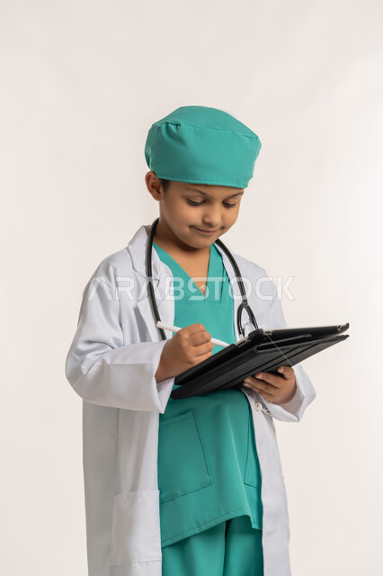 استخدام قلم التابلت للنقر على شيء ما، تدوين نتائج الفحوصات، الهدف والطموح المستقبلي بالعمل في العيادات والمشافي، بورتريه لفتى عربي خليجي اماراتي يرتدي المعطف الأبيض والسماعات يحمل جهاز لوحي، ولد سعودي بقوم بإعداد التقارير الطبيه، خلفية بيضاء