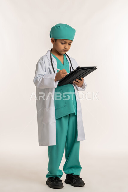 الهدف والطموح المستقبلي بالعمل في العيادات والمشافي، تدوين نتائج الفحوصات، استخدام قلم التابلت للنقر على شيء ما، بورتريه لفتى عربي خليجي اماراتي يرتدي المعطف الأبيض والسماعات يحمل جهاز لوحي، ولد سعودي بقوم بإعداد التقارير الطبيه، صورة لكامل الجسم، خلفية بيضاء