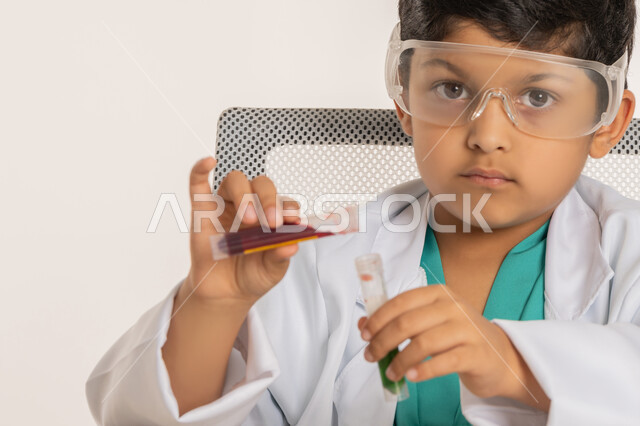 الأبحاث والتجارب العلمية، اختيار وتحديد المستقبل منذ الصغر، مهنة اخصائي مختبرات حيوية، بورتريه مقرب لولد عربي خليجي اماراتي يرتدي المعطف الأبيض يجلس امام الطاولة يضع نظارات واقية يقوم باجراء التفاعلات الكيميائية، فتى سعودي يستخدام أنابيب الأختبار، خلفية بيضاء