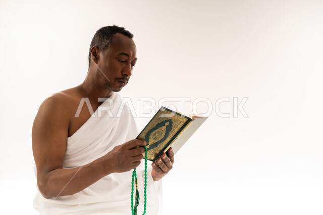قراءة الأذكار والأدعية، حفظ وتلاوة القرآن الكريم، بورتريه مقرب لرجل عربي سعودي خليجي يرتدي لباس الإحرام يحمل بيده السبحة والمصحف الشريف، مفهوم العبادة والتقرب إلى الله تعالى ، سيد عماني يقوم باداء مناسك الحج والعمرة، خلفية بيضاء