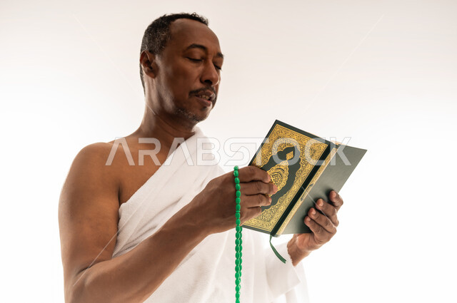 مفهوم العبادة والتقرب إلى الله تعالى، قراءة الأذكار والأدعية، حفظ وتلاوة القرآن الكريم، بورتريه مقرب لرجل عربي سعودي خليجي يرتدي لباس الإحرام يحمل بيده السبحة والمصحف الشريف، سيد عماني يقوم باداء مناسك الحج والعمرة، خلفية بيضاء
