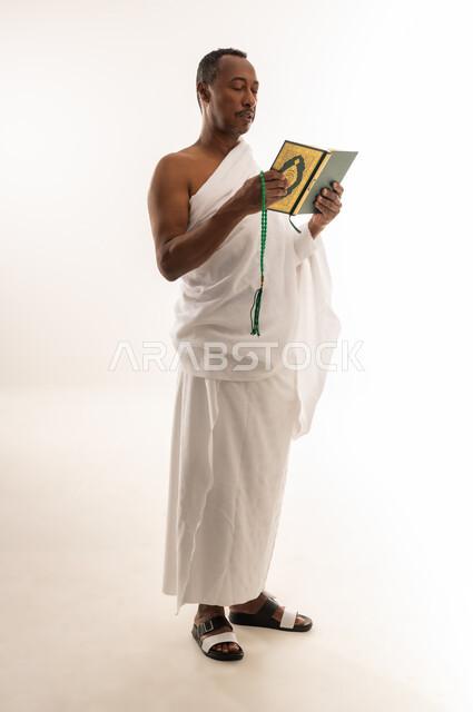 حفظ وتلاوة القرآن الكريم، قراءة الأذكار والأدعية، بورتريه لرجل عربي سعودي خليجي يرتدي لباس الإحرام يحمل بيده السبحة والمصحف الشريف، مفهوم العبادة والتقرب إلى الله تعالى ، سيد عماني يقوم باداء مناسك الحج والعمرة، الجسم بالطول الكامل، خلفية بيضاء